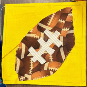 A quilt square showing a football on a yellow backdrop