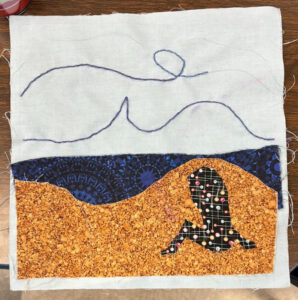 A quilt square with the silhouette of a person on a beach with squiggly blue lines on a white backdrop above the silhouette