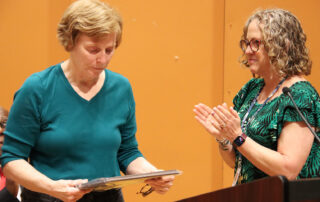 Renee Farrell holds the Paul J. Langan award while Peggy Sinclair-Morris claps.