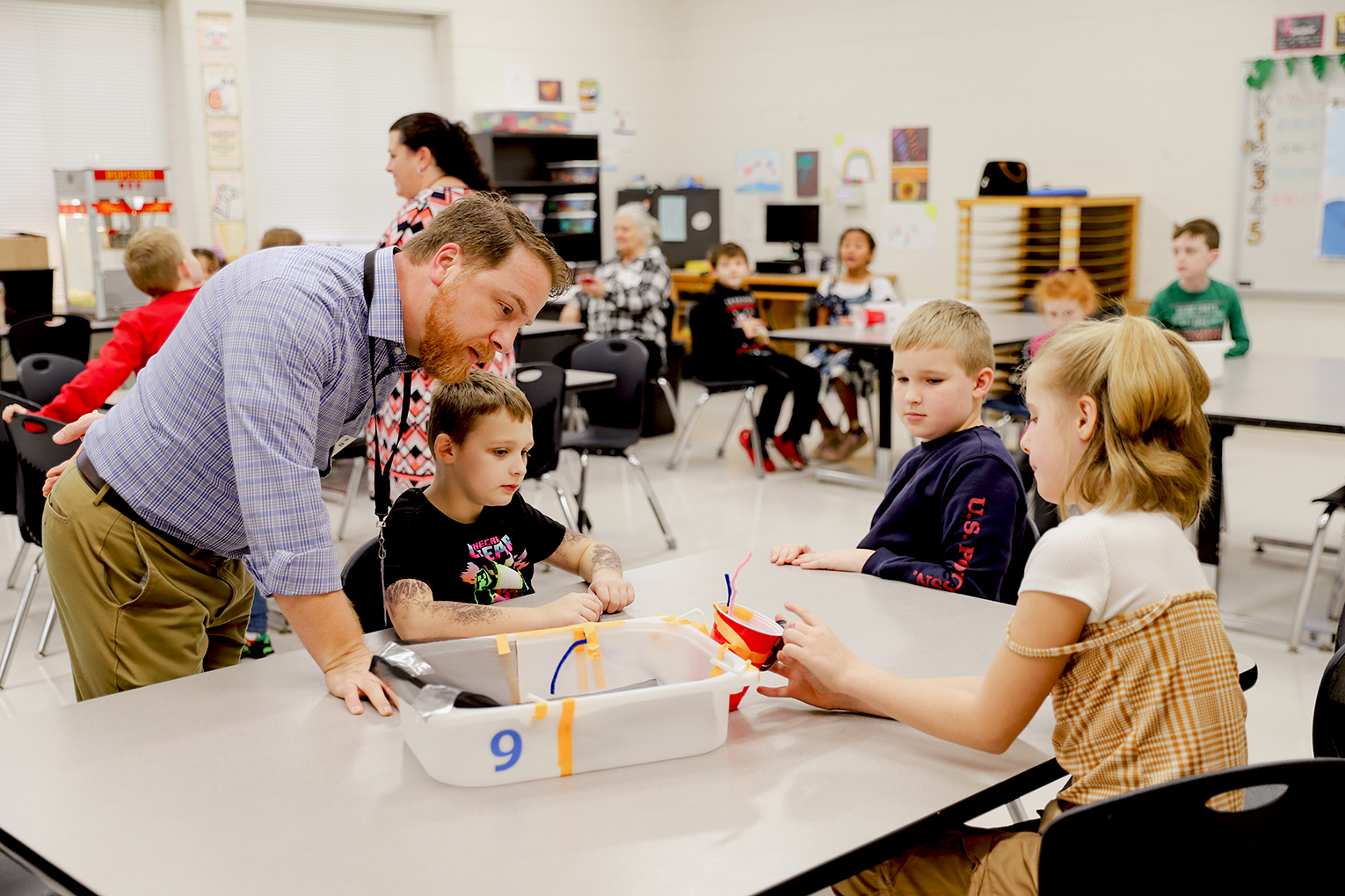 A man helps a table with multiple students as they're working on schoolwork