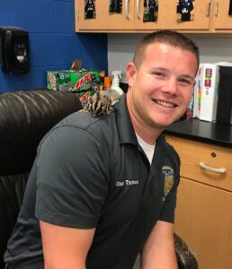 A man sits and smiles with a rodent on his shoulder