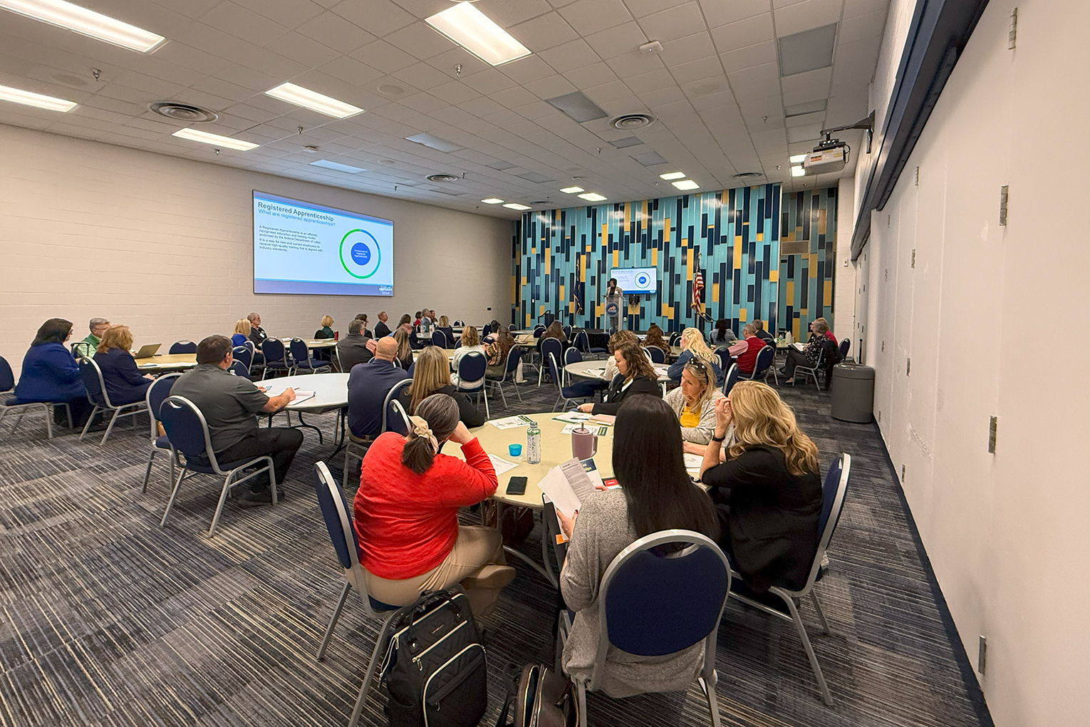 Multiple tables with people sitting around them fill a conference hall