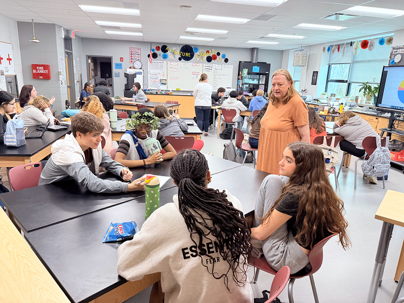 A teacher stands next to a table with students sitting around it in a classroom