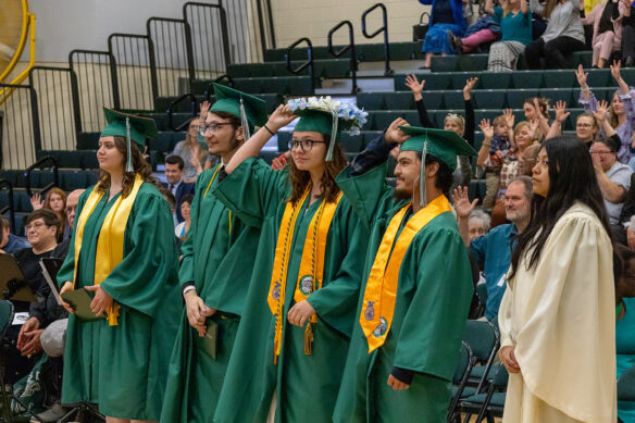 Four students in green graduation gowns adjust their tassels