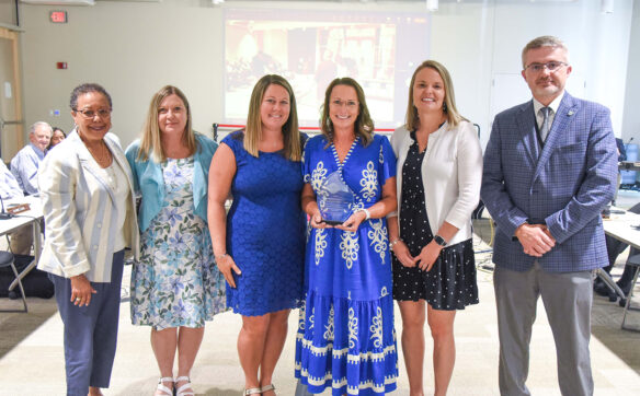 Six people pose for a photo while one hold an award