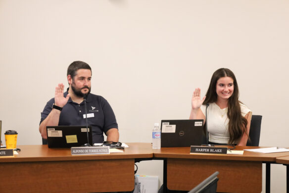 Alfonso De Torres Núñez and Harper Blake sit at a table with their right hands raised.