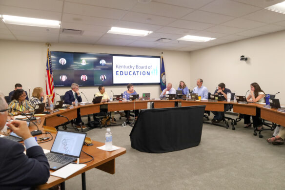 Members of the Kentucky Board of Education sit around a half-circle of tables, talking.