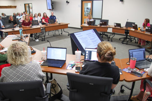 Elizabeth Dinkins sits at a table and speaks to members of the Education Professional Standards Board, who are seated in a semi-circle of tables around Dinkins