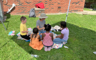 A group of kids sit around a woman in a grassy field
