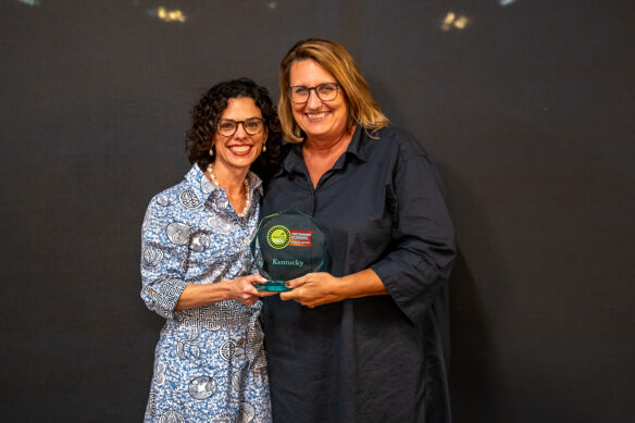 Kimberly Woodall and Chelle Travis smile for a photo together, holding an award in their hands