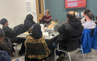 A group of people meet in a room, sitting around a table