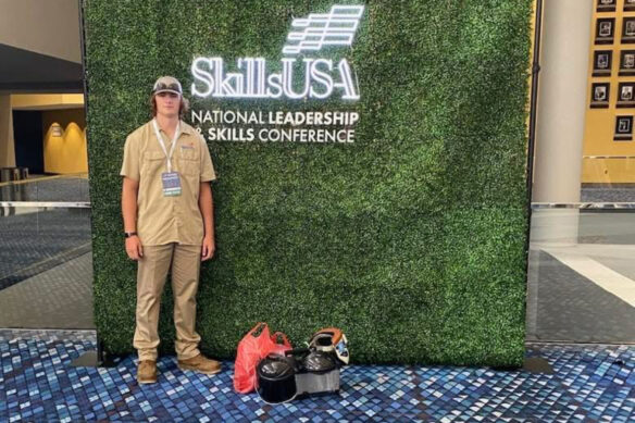 Trevor Ellis stands in front of a sign that says SkillsUSANational Leadership and Skills Conference