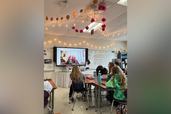 A man on a projection screen speaks to a classroom of kids