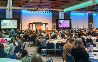 Several tables fill a ballroom with people sitting at them