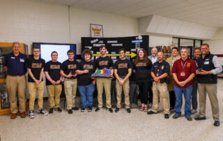 A group of people pose for a photo, with one of the people in the center holding an STLP award that feature the STLP logo over an outline of Kentucky