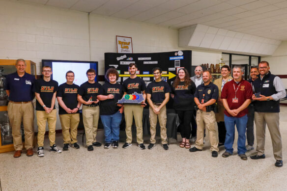 A group of people pose for a photo, with one of the people in the center holding an STLP award that feature the STLP logo over an outline of Kentucky