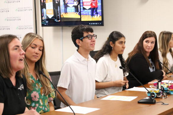 A group of people sit at a table and talk into microphones