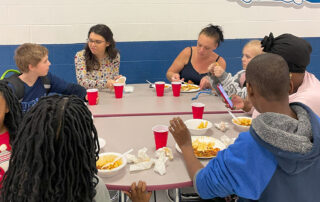 A group of people sit around a table with food and red cups
