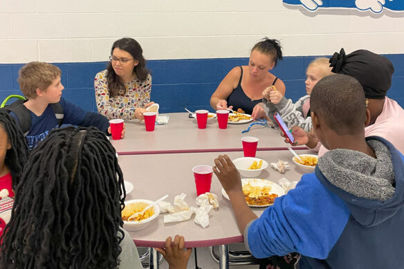 A group of people sit around a table with food and red cups