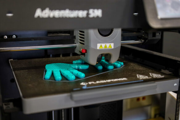 Close up of a 3D printer working up a set of hands that are made of a teal-colored material