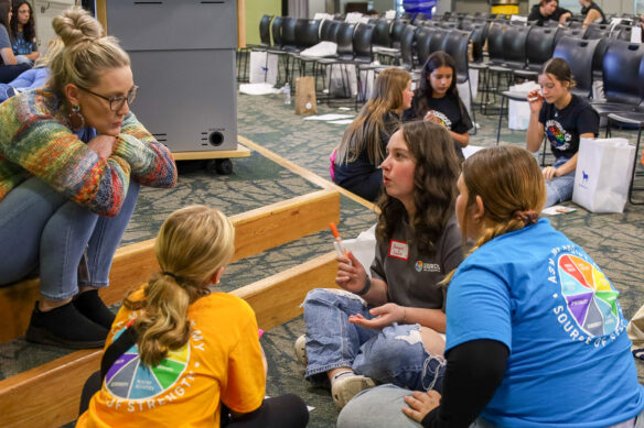 A group of people sit around on the floor and talk to each other