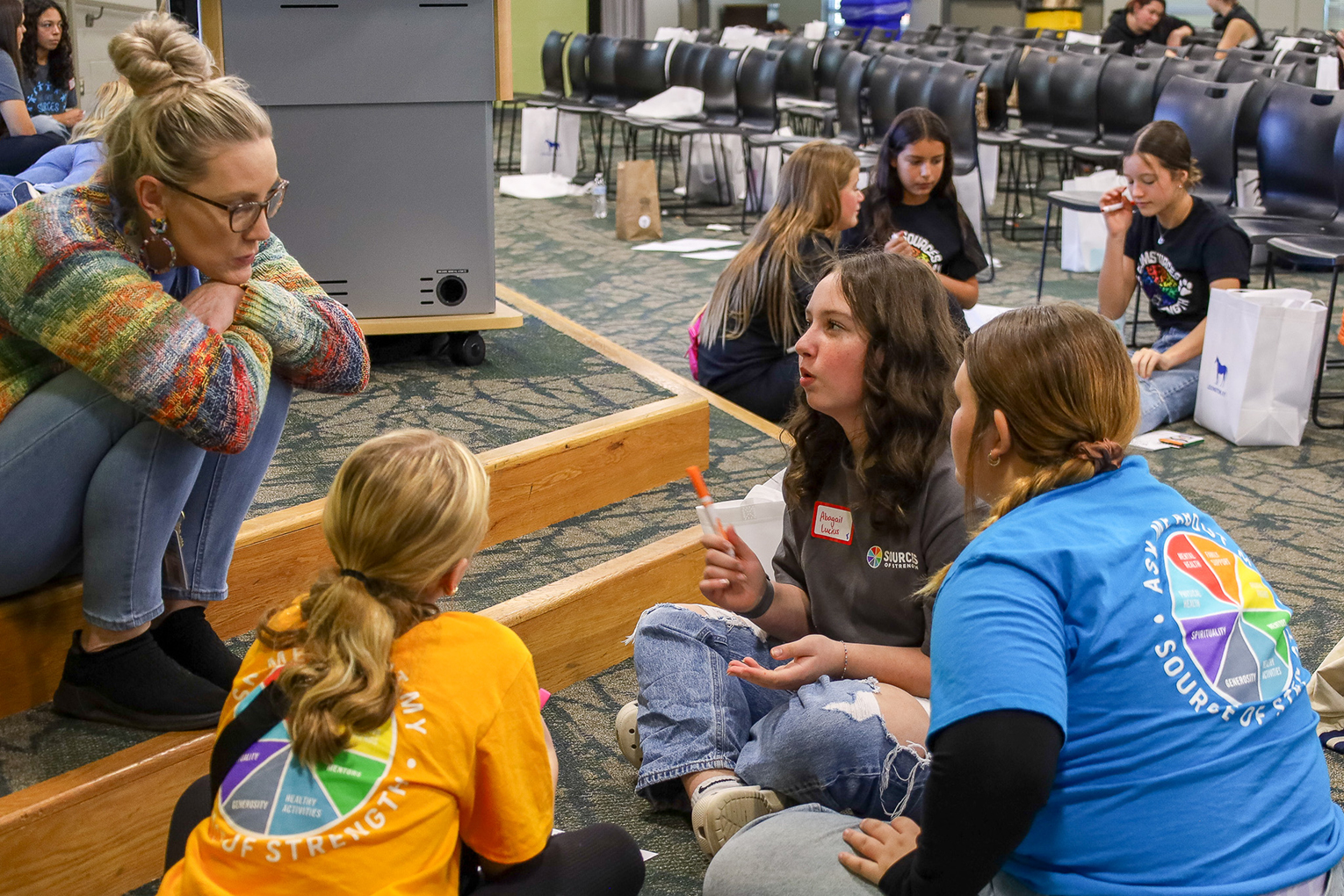 A group of people sit around on the floor and talk to each other