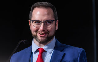 A man in a blue suit speaks into a microphone