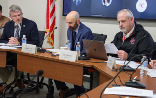 Robbie Fletcher speaks to two men who are sitting at a table with Robbie. One of the men is reading a piece of paper