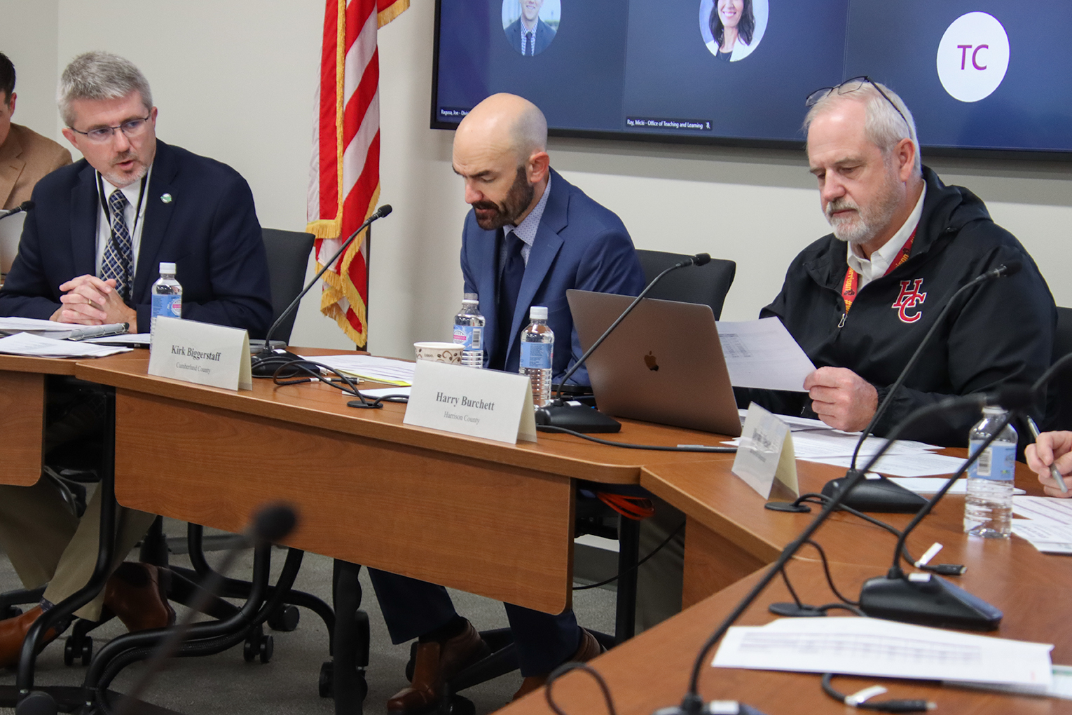 Robbie Fletcher speaks to two men who are sitting at a table with Robbie. One of the men is reading a piece of paper