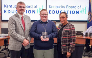 Three people stand and smile for a photo, one of whom is holding an award