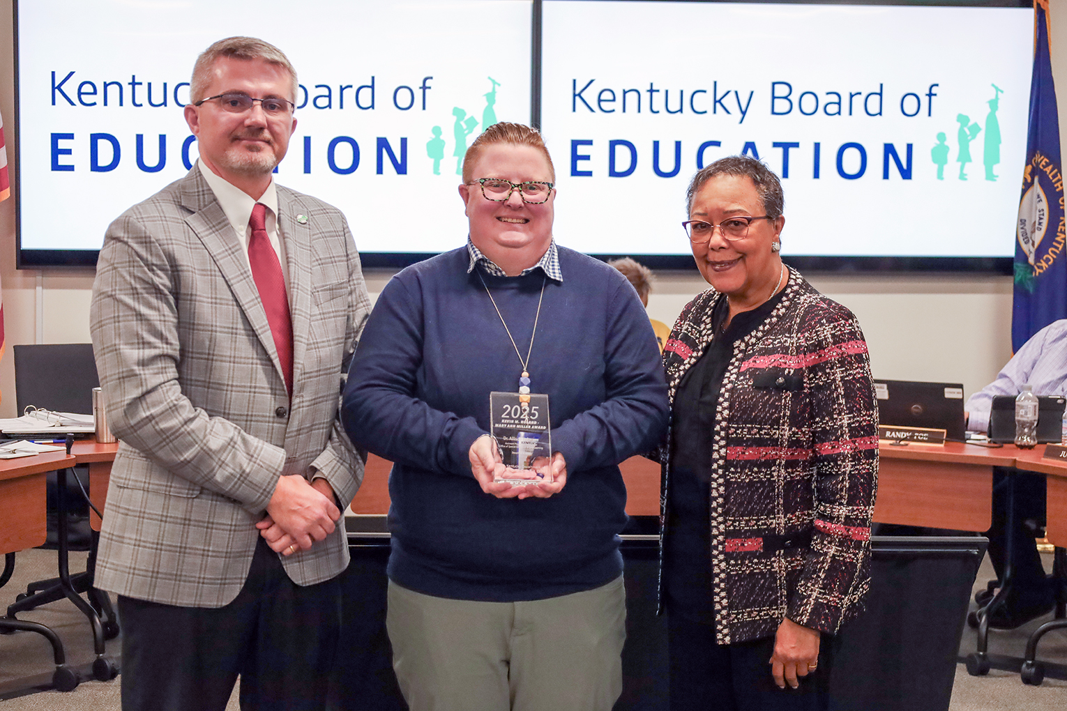 Three people stand and smile for a photo, one of whom is holding an award