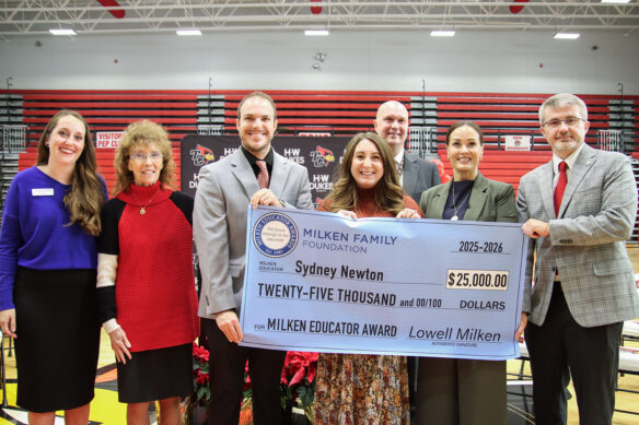 Sydney Newton stands holding a large ceremonial check for $25,000 with people surrounding her.
