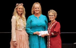 Three women pose for a photo as the woman in the middle holds a glass award