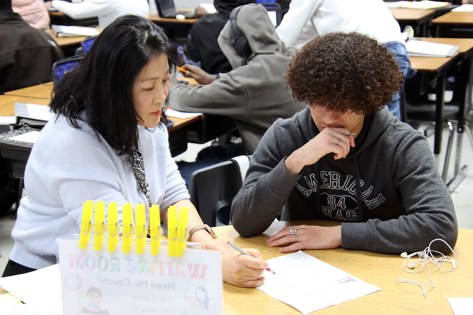 a woman sits down with a student, putting a red pen to a piece of paper