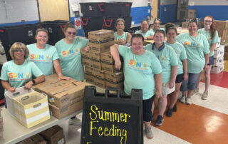 Smiling members of the Owen County summer meals program stand by boxes of food to be given out to children.
