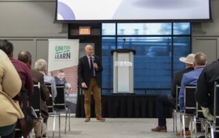 Man standing in front of crowd with a microphone addressing questions