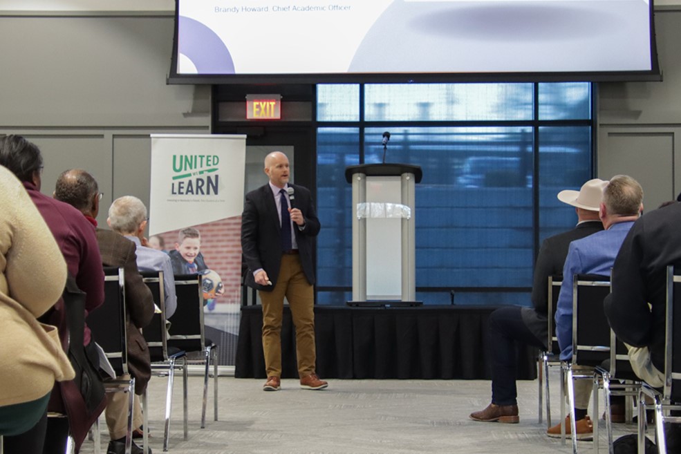 Man standing in front of crowd with a microphone addressing questions