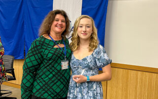 Two people pose for a photo together as one of them holds a glass award
