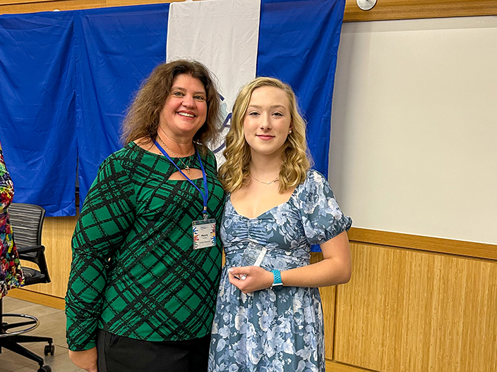 Two people pose for a photo together as one of them holds a glass award