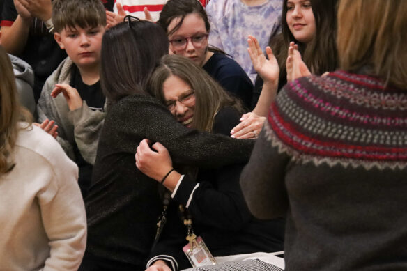 Two people hug amid a crowd of others on the bleachers of a gymnasium