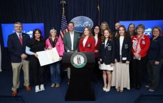 group of students and adults around a podium holding a proclamation signed by the Governor of Kentucky.