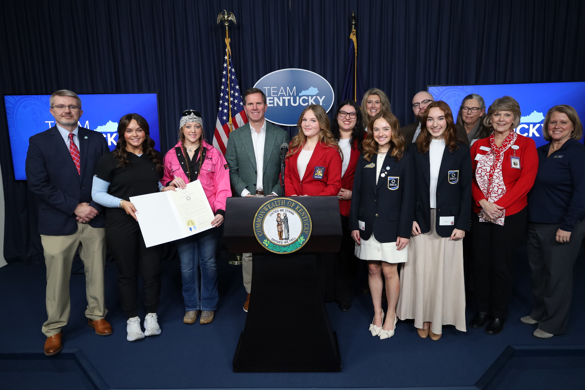 group of students and adults around a podium holding a proclamation signed by the Governor of Kentucky.