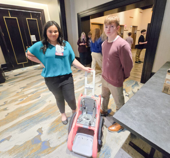 Two students stand next to a wheel chair that they 3-D printed