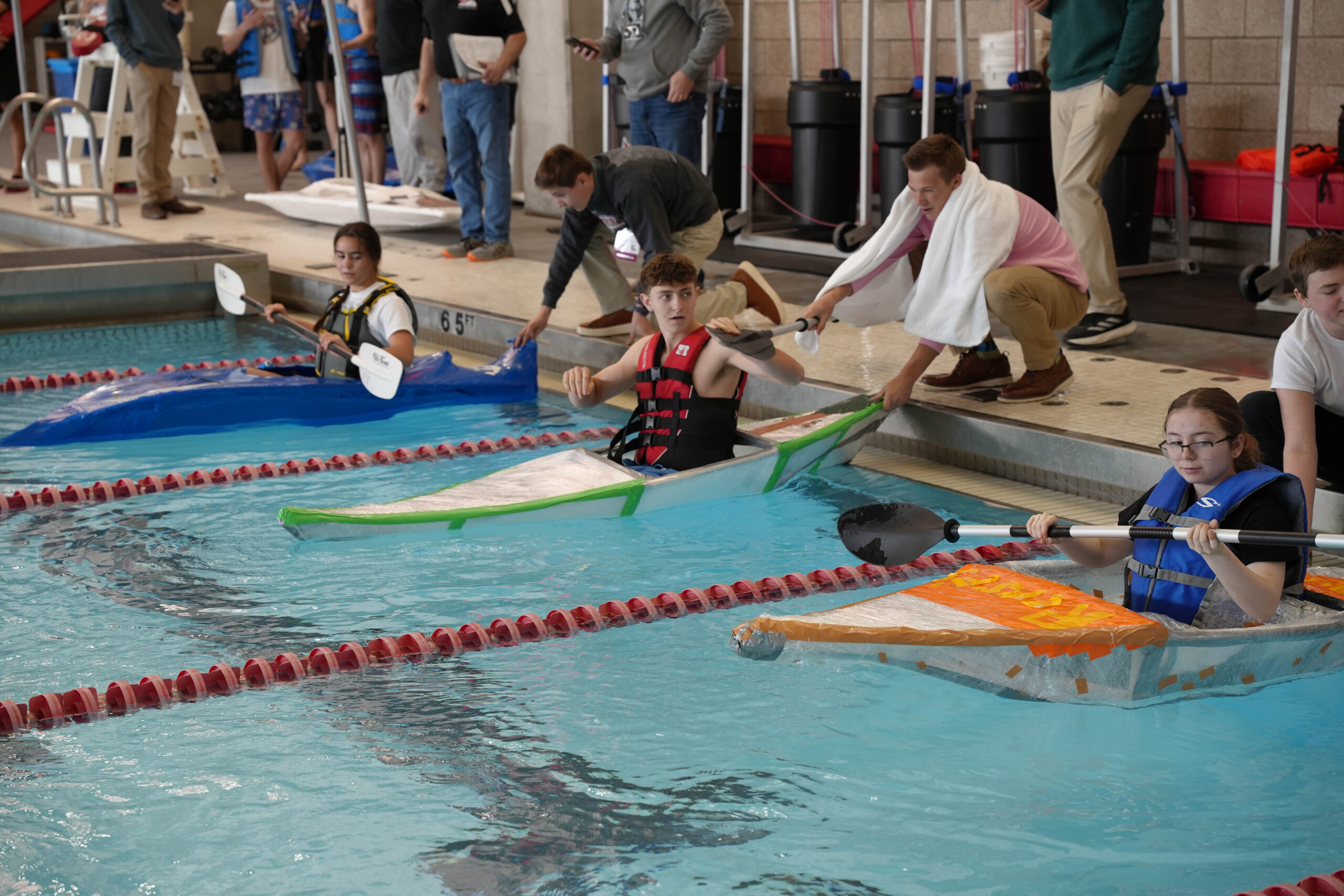 three kayaks piloted by students in a swimming pool