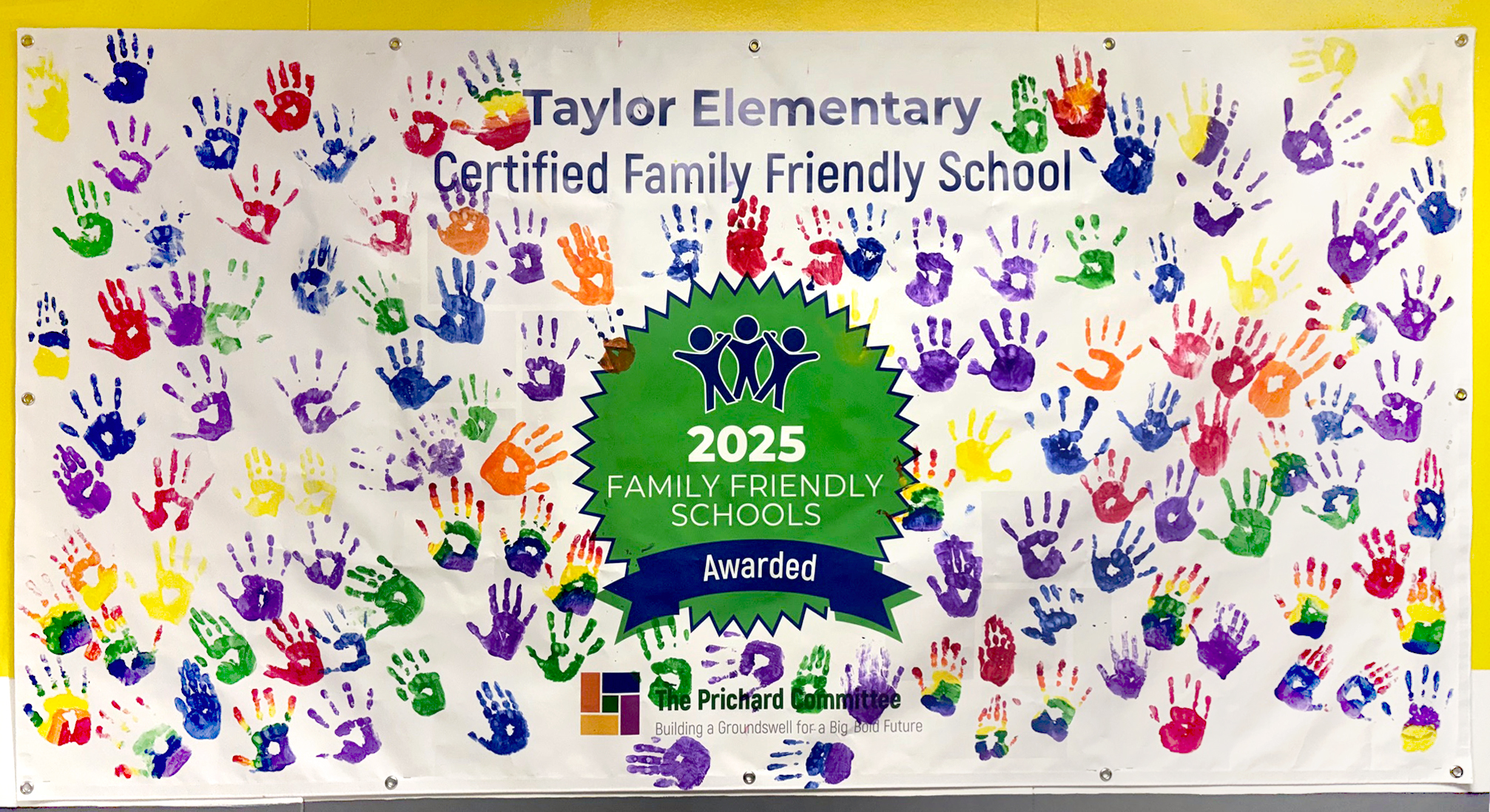 A mural with handprints in different colors and the words "Taylor Elementary Certified Family Friendly School" on it