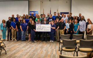 A group of dozens of people pose with a few people in the middle holding a giant check