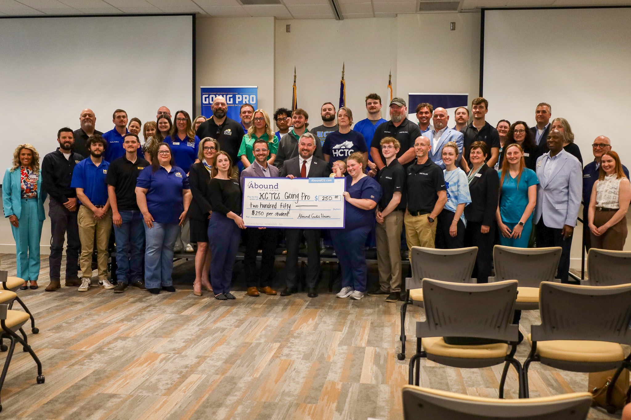 A group of dozens of people pose with a few people in the middle holding a giant check