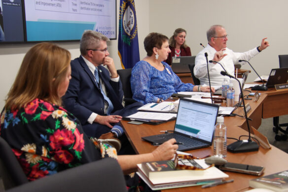 A man holds his hands out demonstratively as three others sitting next to him and another woman sitting behind him look at him