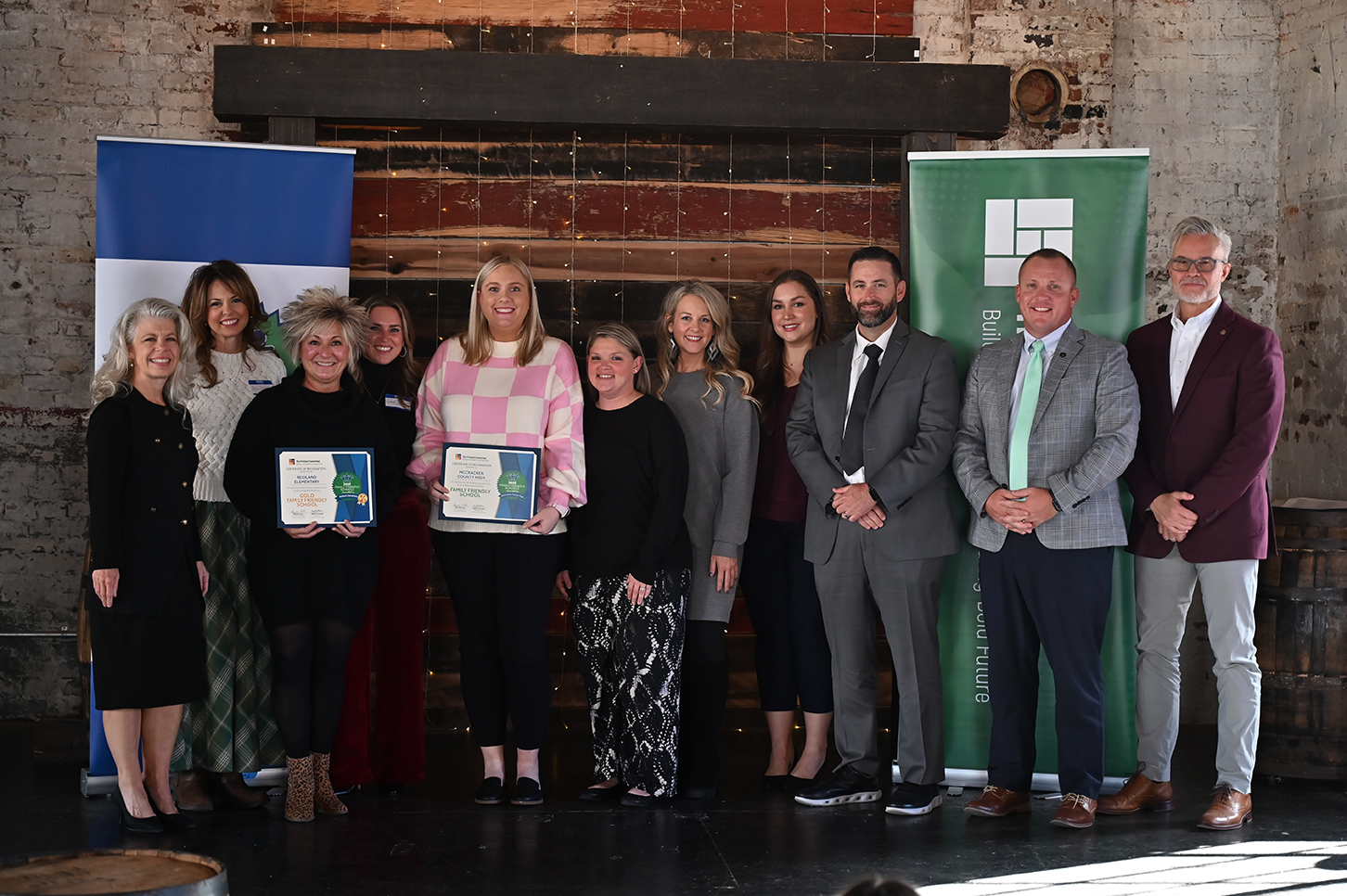 A group of people pose for a photo, and a couple people are holding certificates