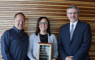 Three people pose for a photo while a woman in the middle holds an award